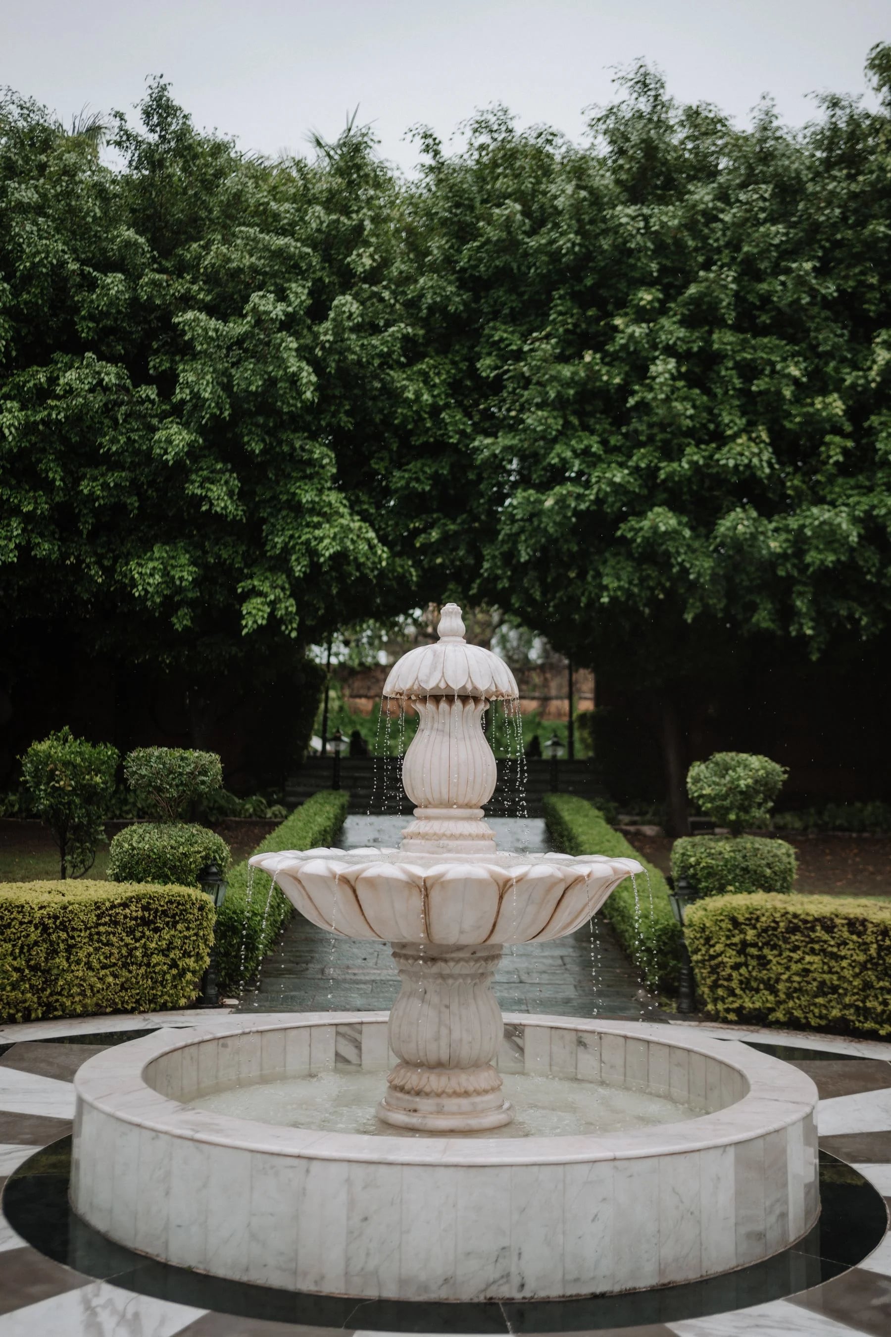 White marble water fountain with carved basins and flowing water in a landscaped garden